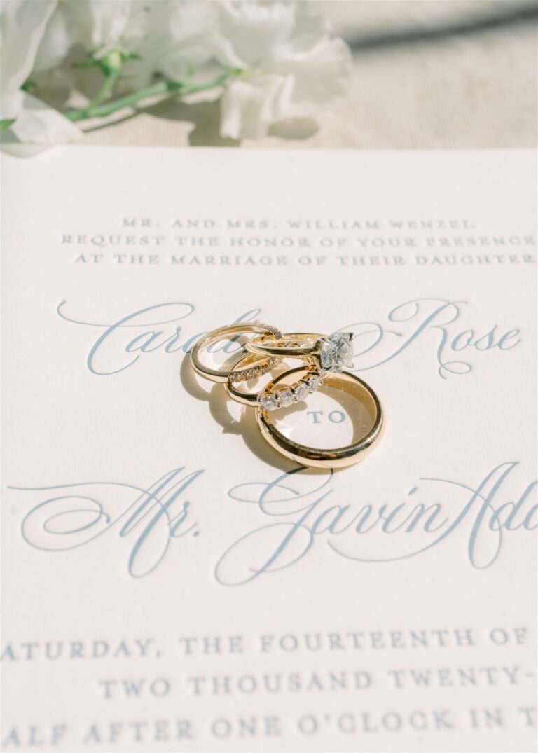 Gold wedding rings sitting on an elegant white and blue letterpress invitation card